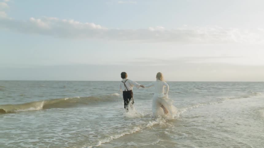 Two children run out into the water on the beach