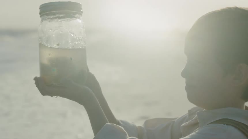 Child examines a jar of water with objects in it