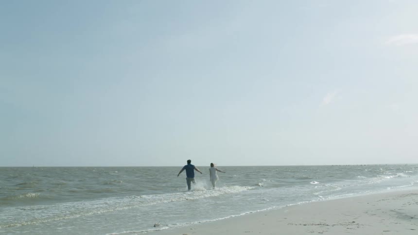 A man and woman run into the ocean fully clothed