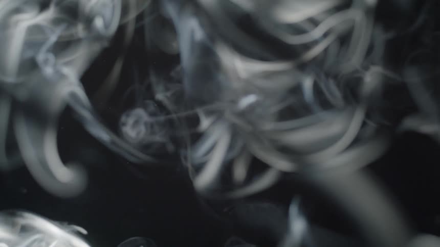 Smoke billows in the light and a dark background