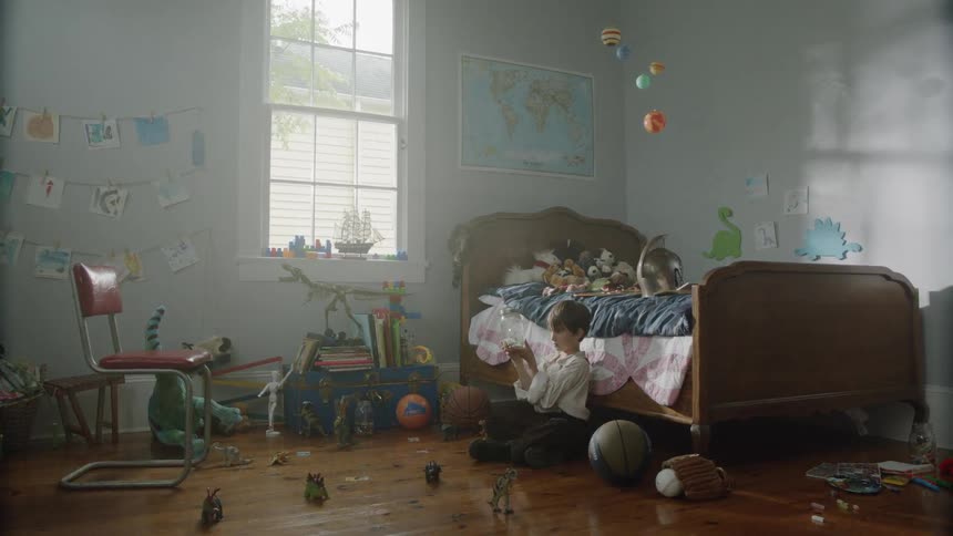 A boy is sitting on the floor in his room shaking a glass jar and looking at it