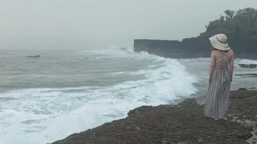 A woman stands on a beach as waves crash ashore