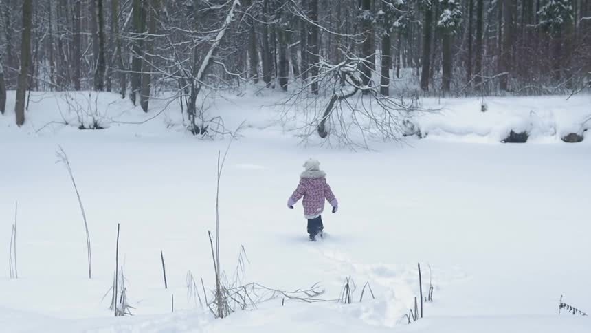 A kid is walking through some deep snow towards the tree line