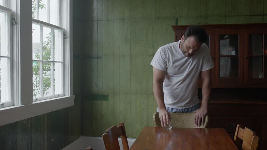 A man leans on a chair and puts his glass on the table