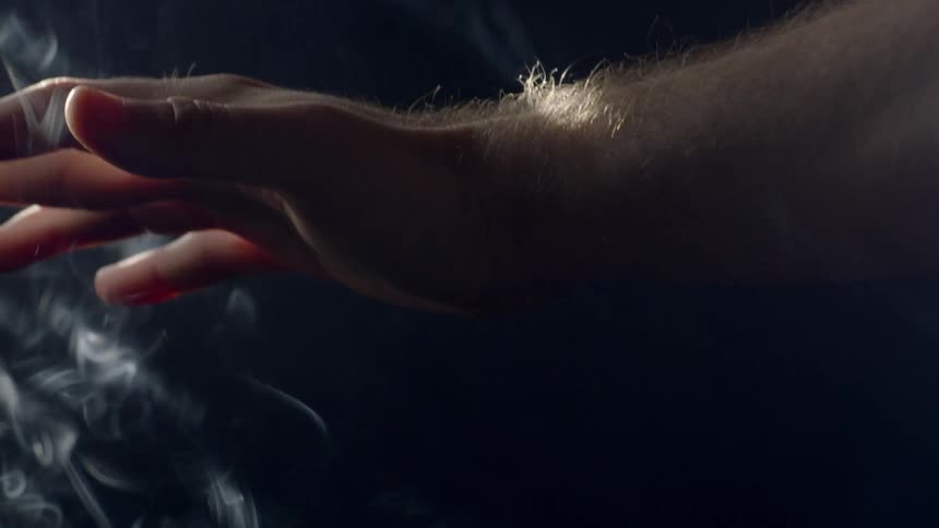 A man moves his hand up and down in smoke and sunlight