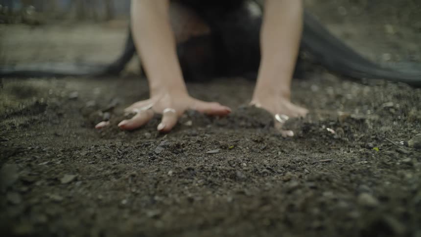 A woman presses her hands down in the soil on a windy day