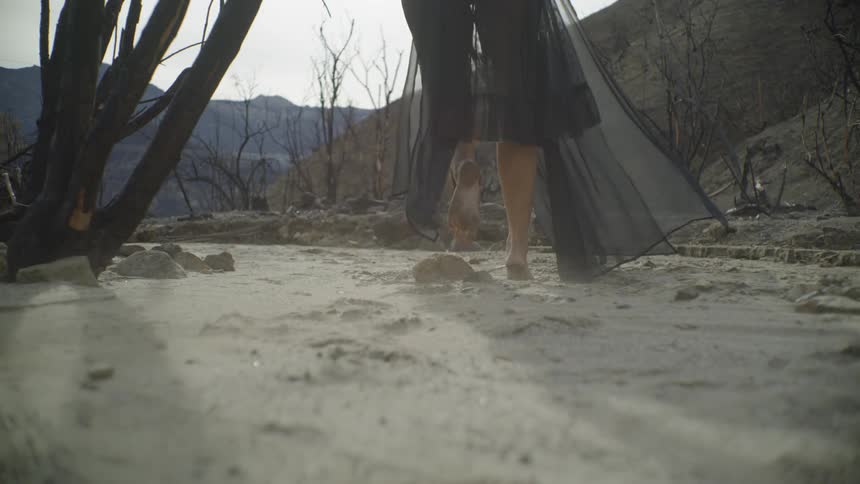 A person walks barefoot in the sand on a cloudy day