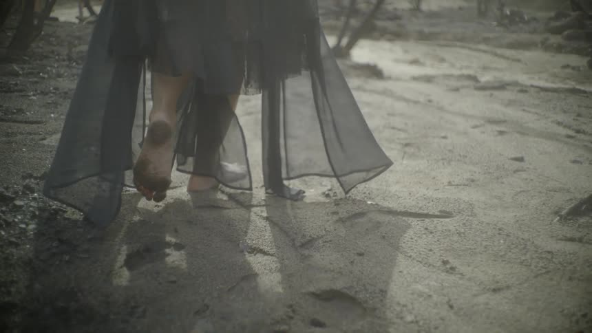 Woman wearing a black lacy dress walks outside in the sand