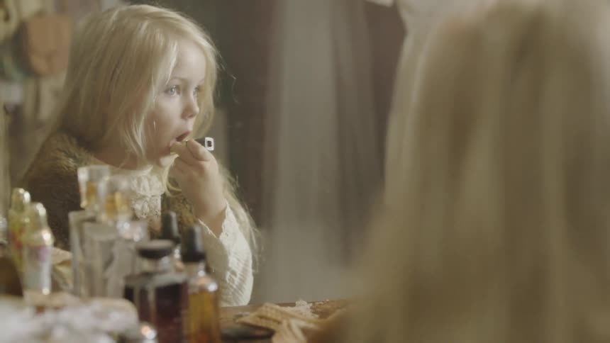 Child walks up to a vanity and puts lipstick on