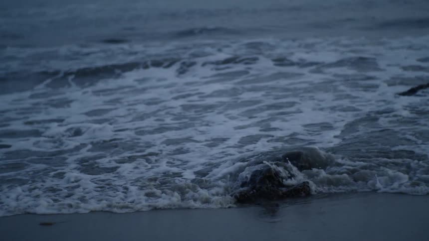 The waves splash and crash against the rocks and sand at sunset