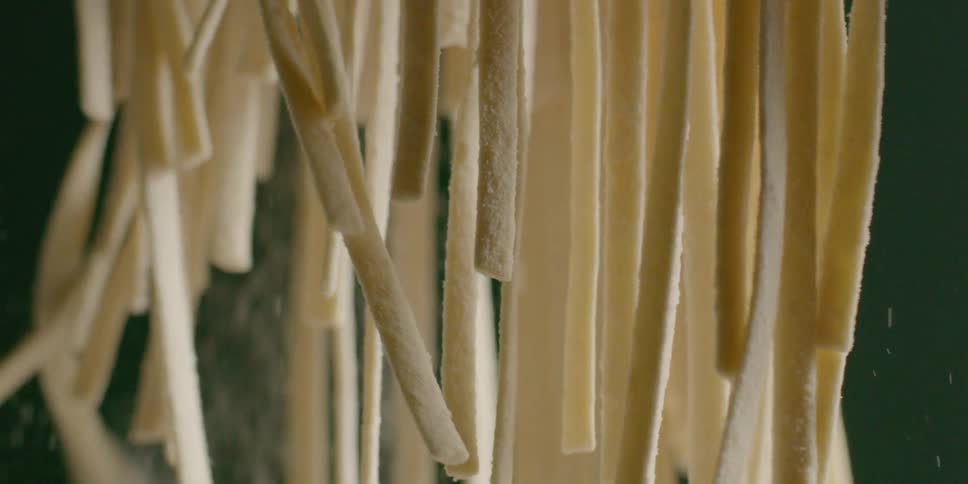 Flour is being thrown onto pasta noodles as they dangle in the air