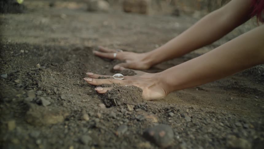 A woman rubs her hands across the dirt ground