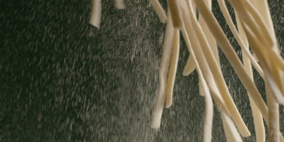 A chef holds strands of raw pasta