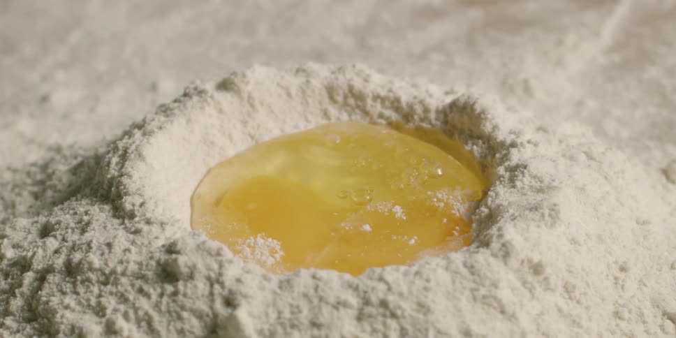 An egg is dropped into the center of piled flour