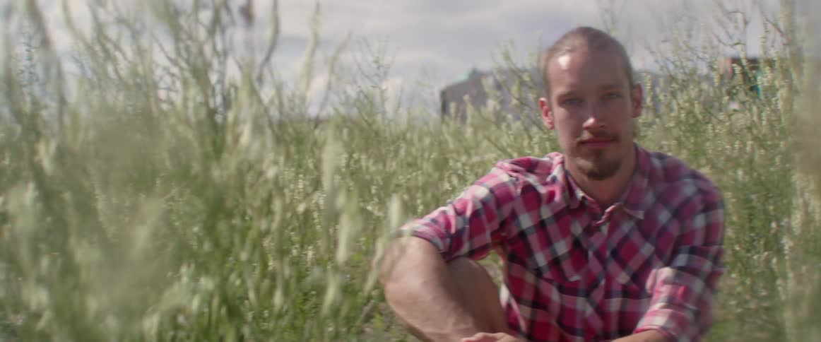 An adventurer pauses his outdoor hike to sit in a green meadow.