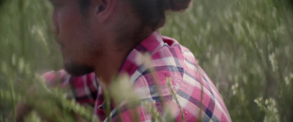 A thoughtful traveler pauses his walk to sit among high weeds outdoors alone.