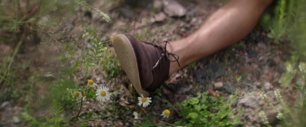 Man in casual shoes sitting on the ground amongst small flowers