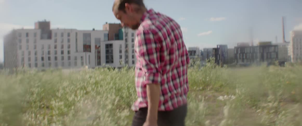 A traveler walks through overgrown grass near a building development site in daylight.