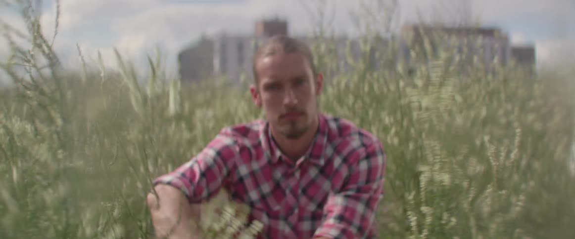 A thoughtful male adventurer rests on the ground among high wild weeds alone.