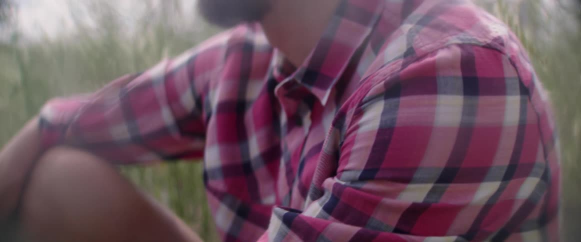 A person wears a colorful button down shirt while resting in a meadow.