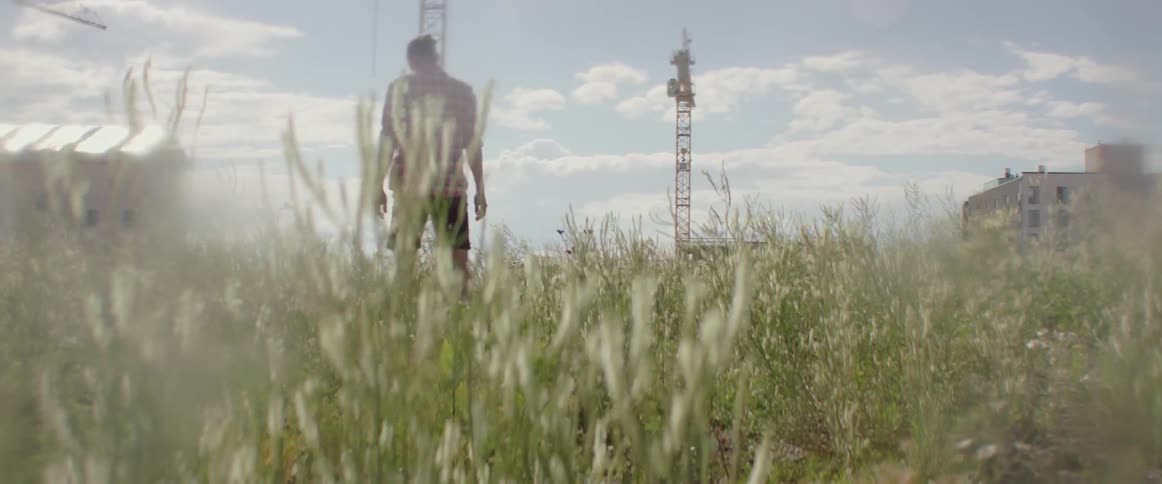 A young man signals someone while exploring a wild field of green grass.