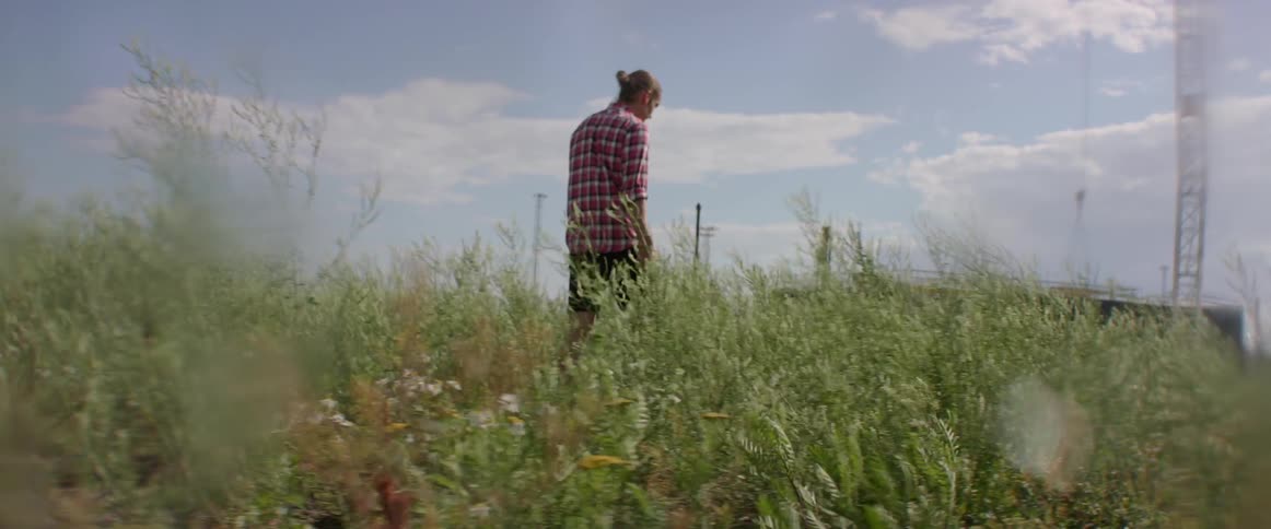 A male traveler walks through high grass while enjoying a sunny day outdoors
