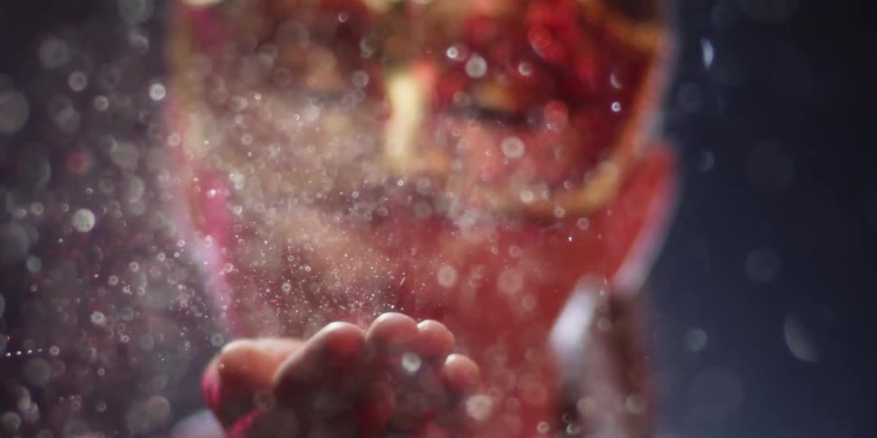 A masked person blows glitter from the palm of their hand