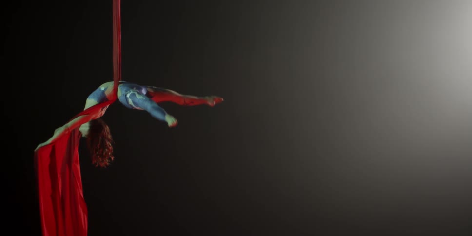 Woman twirls around in midair holding on to a red cloth