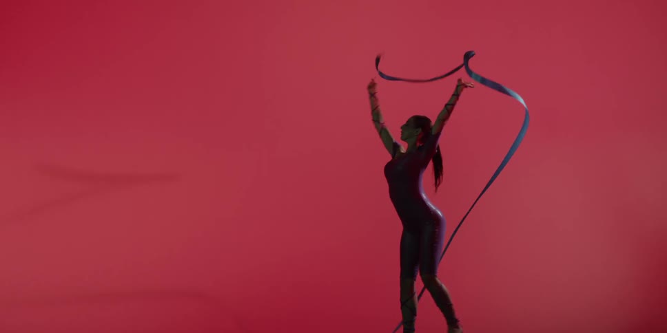 A woman is ribbon dancing against a red backdrop