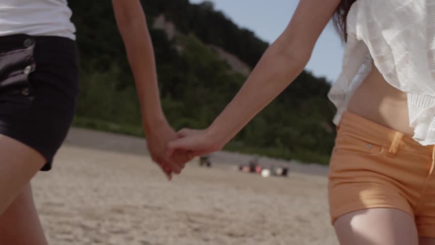 Two women hold hands while walking on the beach