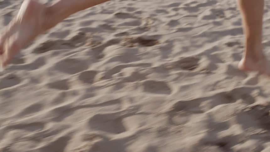 A person's legs and feet as they run on the beach