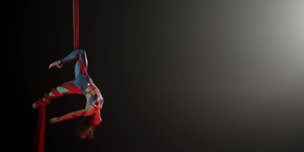 An acrobat glides down a ribbon while suspended in air