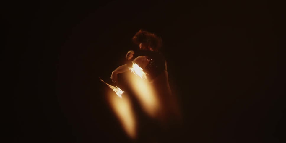 Woman spins two fire lit objects around in the dark