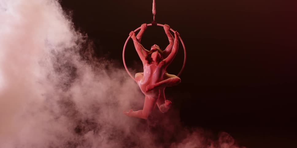 Smoke rises around two women twirling on an aerial hoop