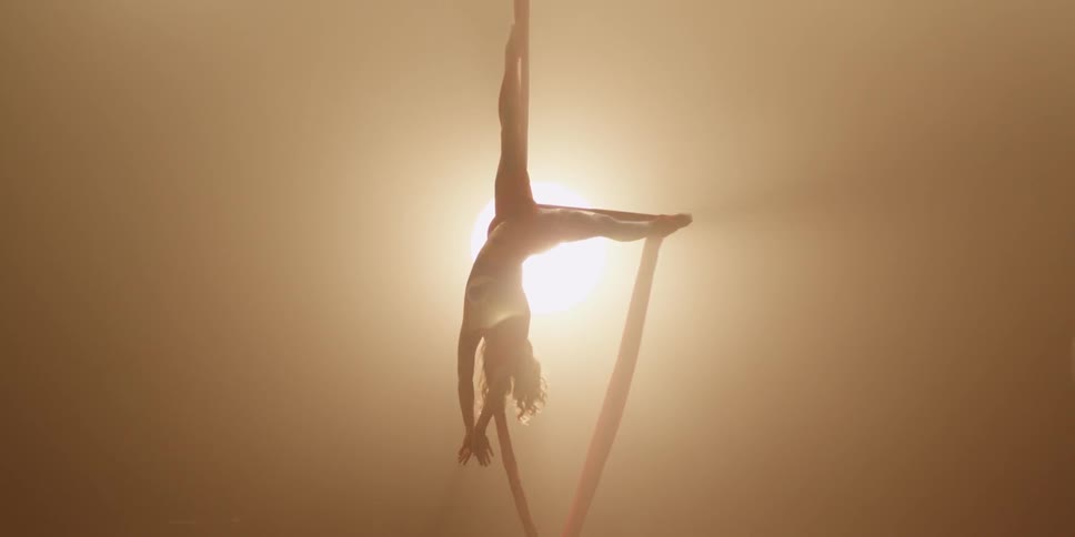An acrobat spins upside down on a ribbon