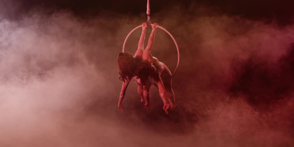 Two women perform suspended in the air on a hoop with a dark smoky background