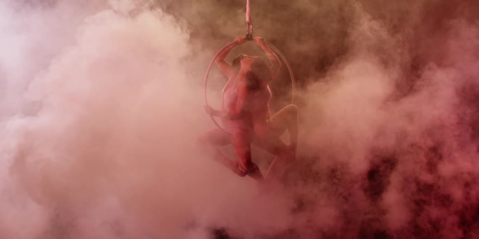 Two people are sitting on a suspended circle in a room filled with smoke