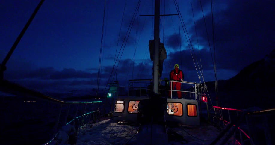 A man stands on a boat and looks ahead at night