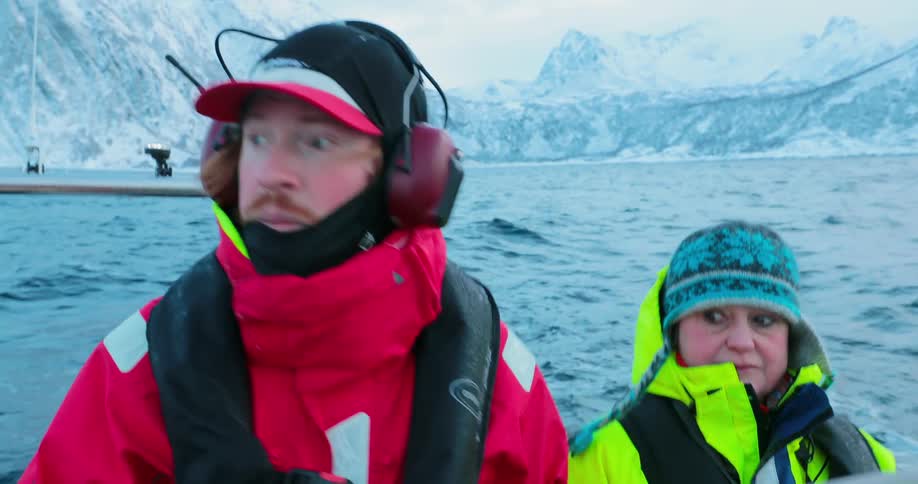 People ride in a boat off a snowy shoreline
