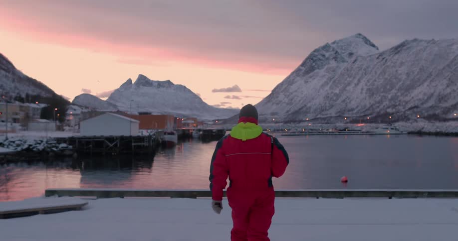 A man walks on a snowy dock at sunset