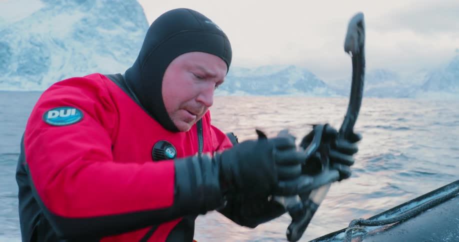 A diver is sitting on the edge of a boat putting on diving equipment