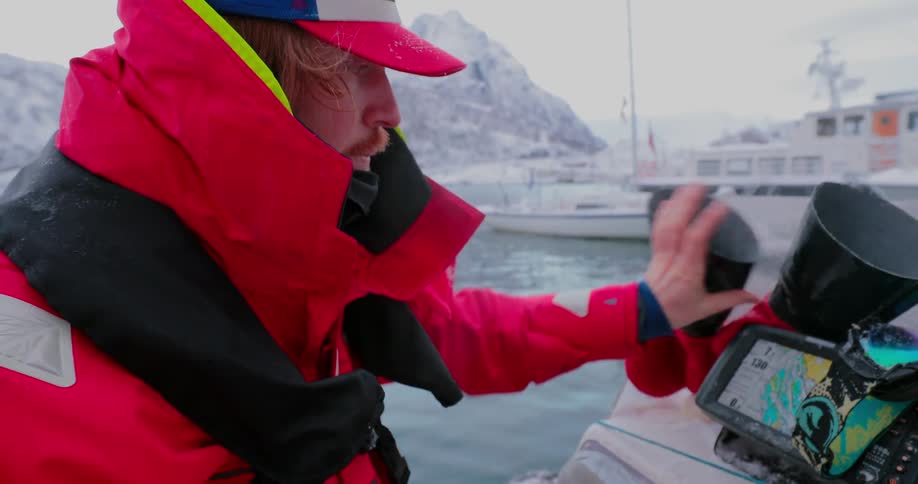 A man is bundled up on a boat on the icy water