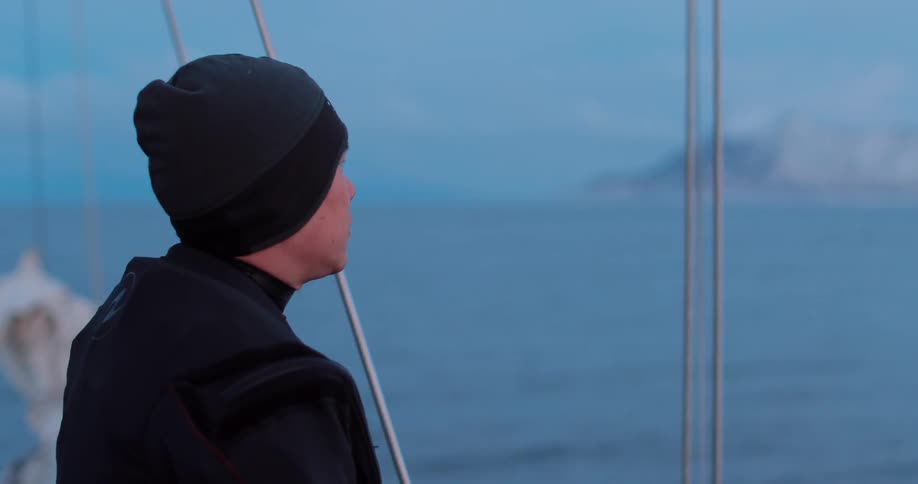 Man wearing a knitted cap looks out at the waters from the side of a boat