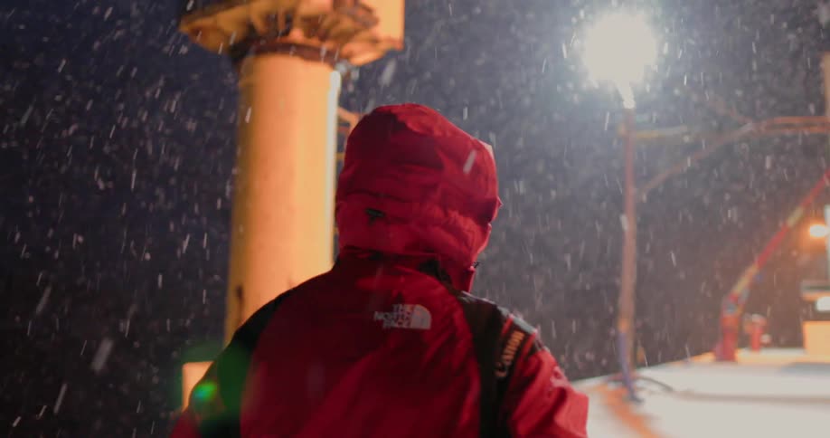 A man with his hood up walks through the snow at night