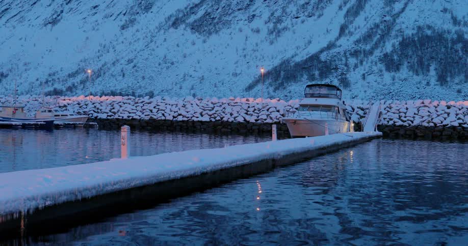 A boat floats next to a snowy dock at dusk