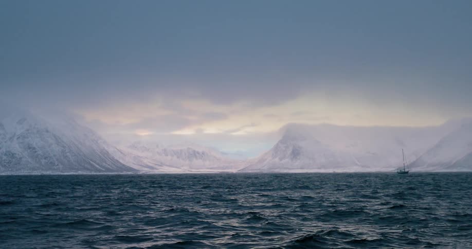 Choppy ocean water with a ship, glaciers and clouds in the distance