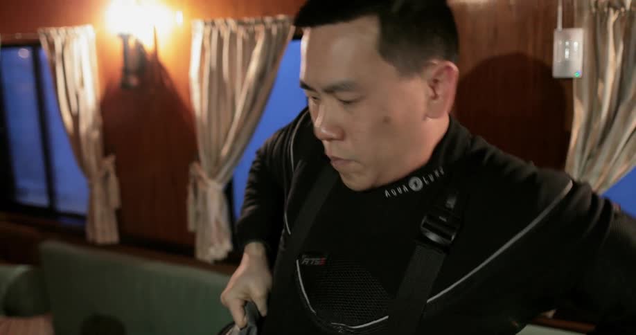 A man in a boat cabin pulls up the straps of his snow pants as he puts them on