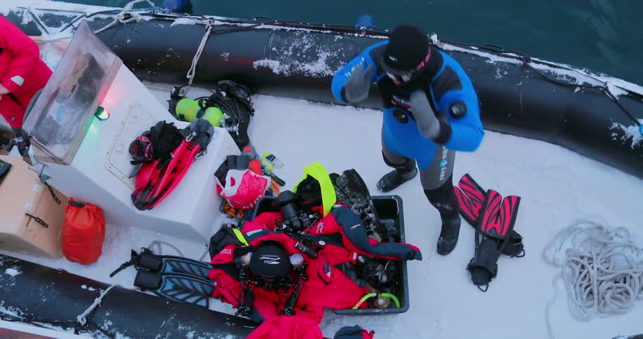 Two people stand in a snow covered rubber raft amid their water gear