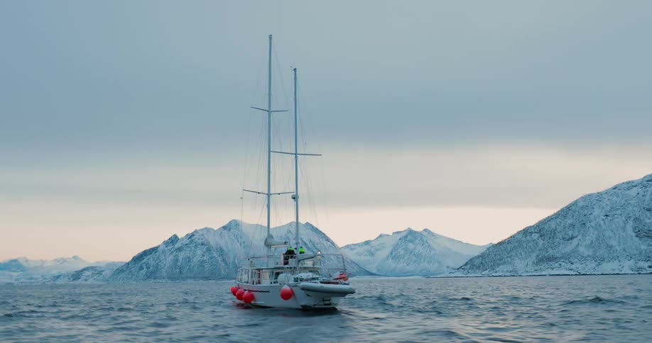 A sailboat is sailing towards a mountainous coastline on a winter day