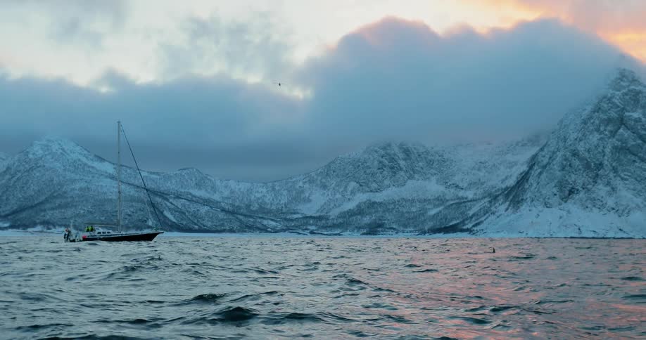 A boat sails off a snowy coast at sunset